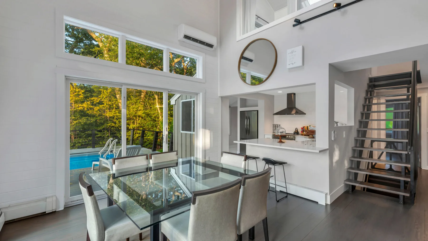 A bright dining area with a glass table, large windows, and a kitchen counter.