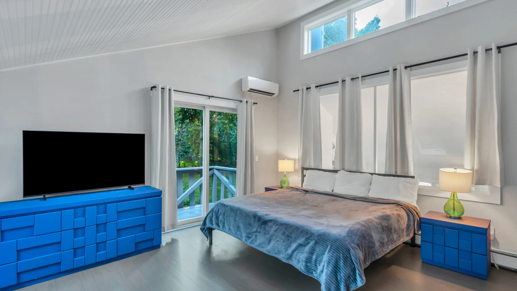 A bright bedroom with a bed, blue storage furniture, and large windows.