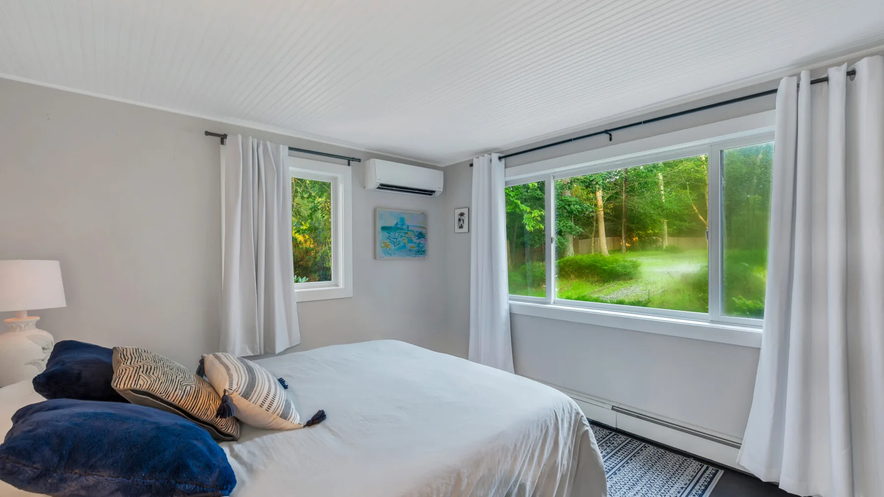 A bedroom with a bed beside large windows overlooking a green garden.