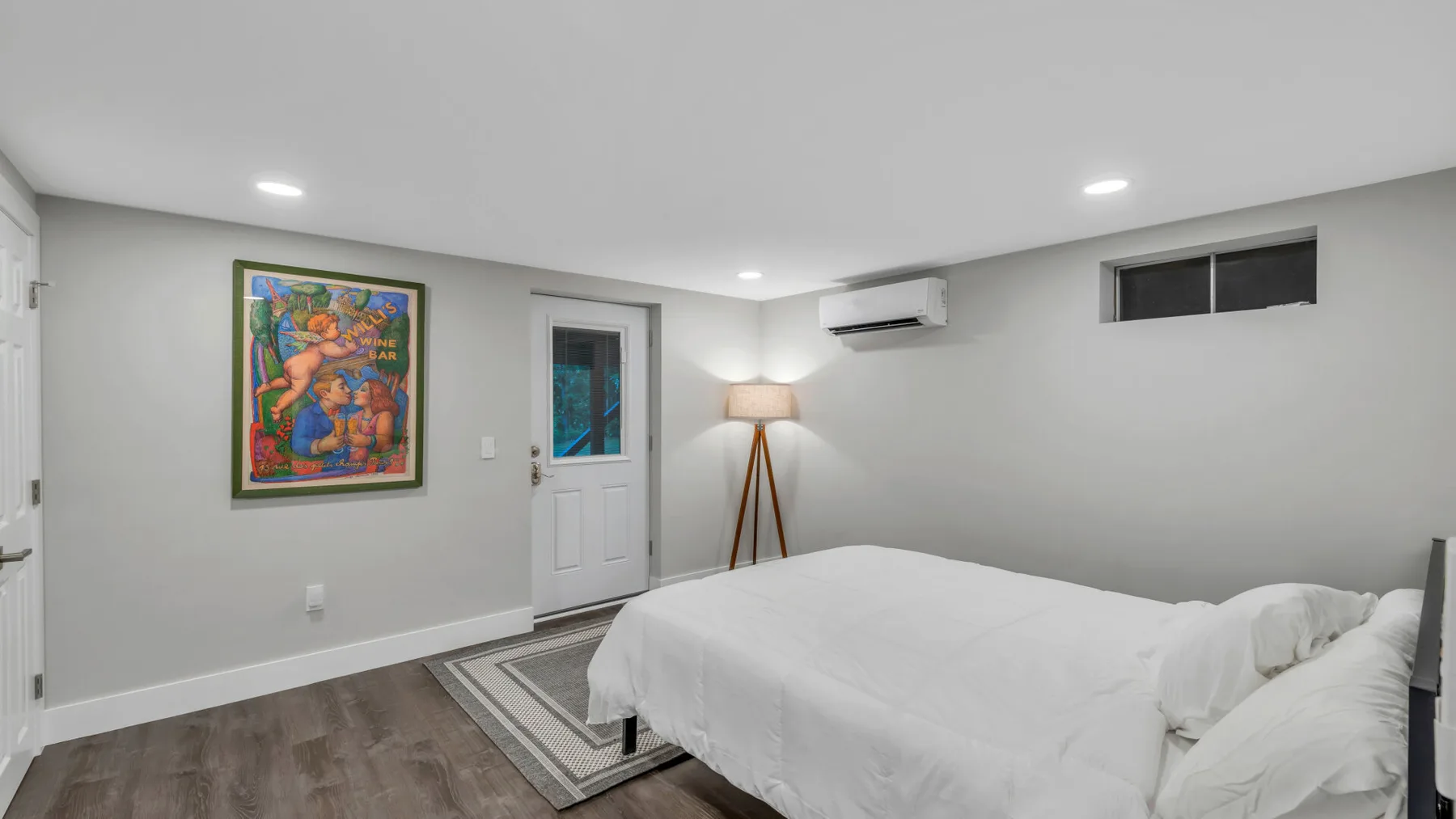 A bedroom with a neatly made bed, colorful wall art, and a floor lamp.