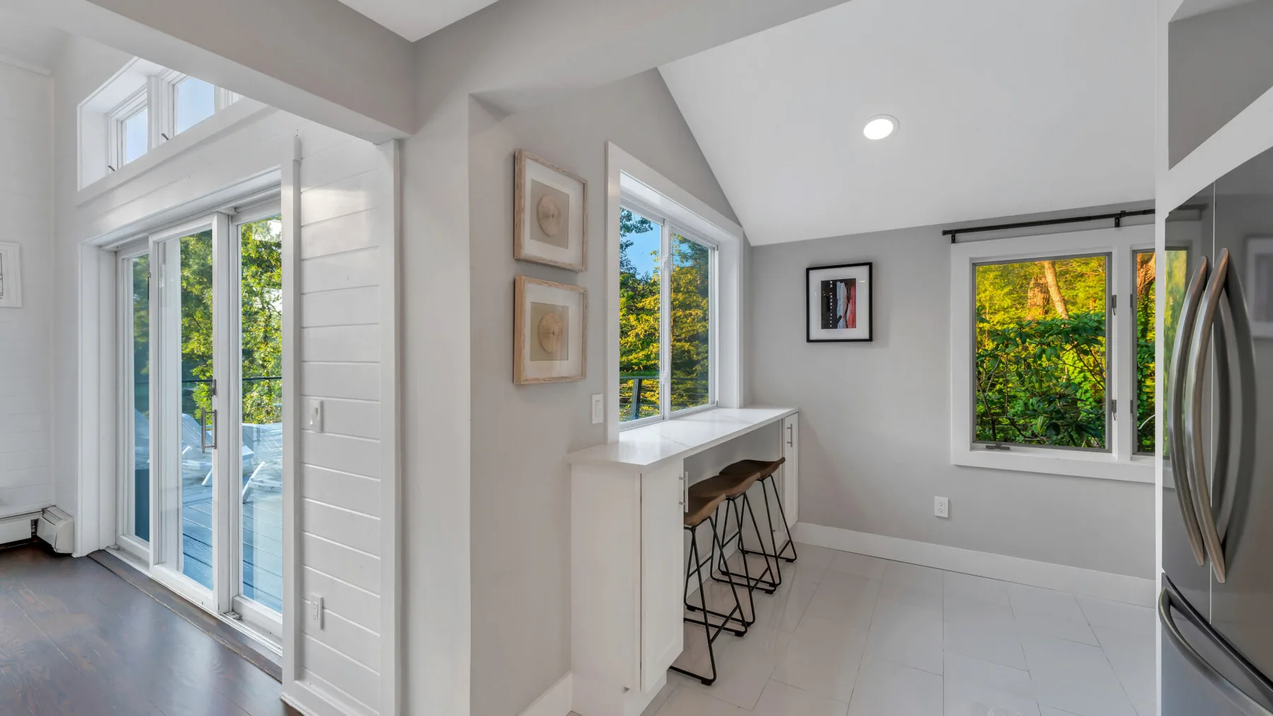 A bright kitchen nook with a counter and windows overlooking leafy greenery.