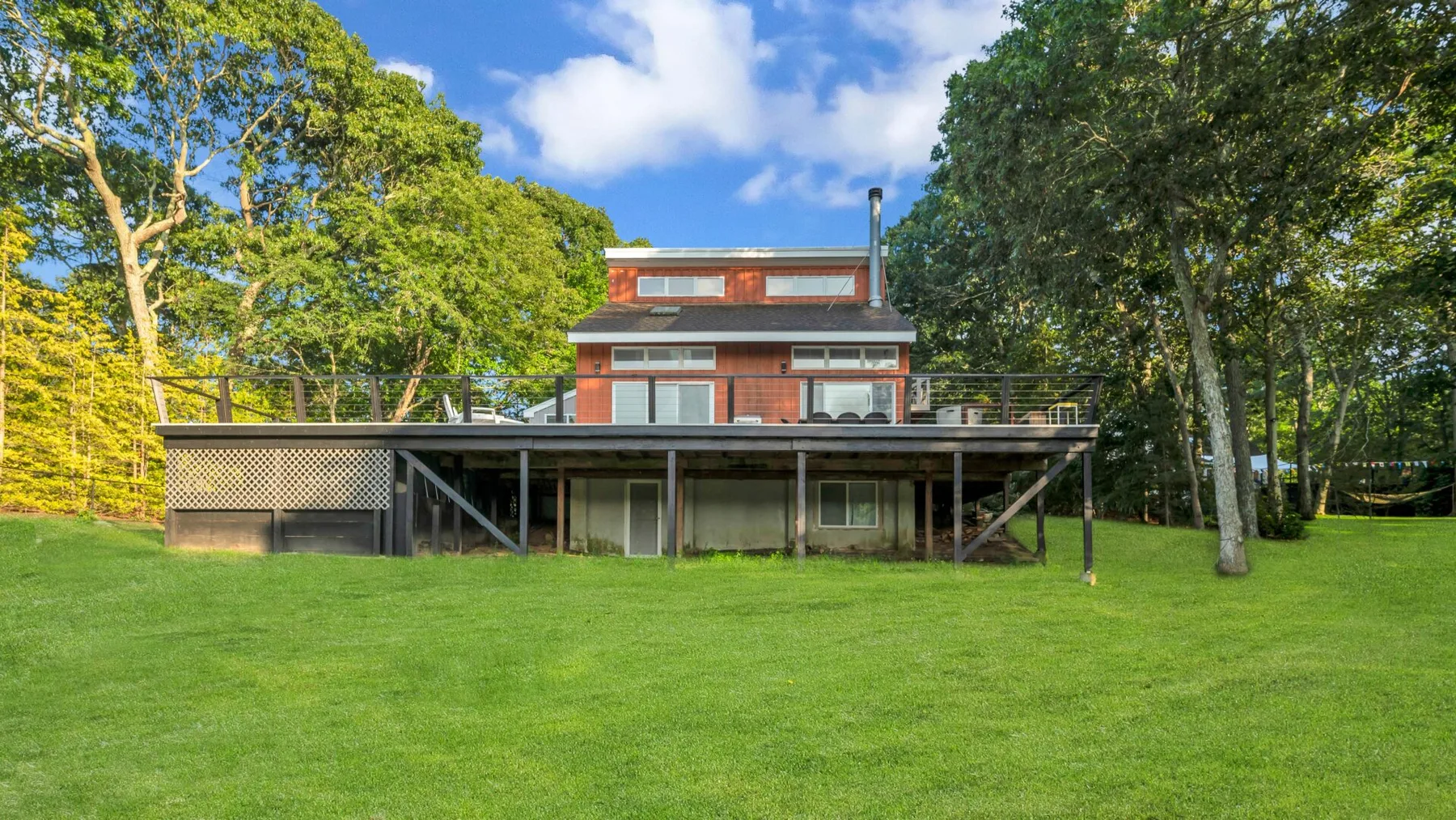 A modern house stands beyond a broad green lawn, surrounded by trees.
