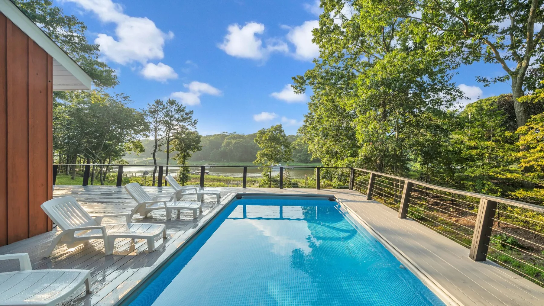 An outdoor swimming pool sits beside a wooden deck and leafy trees.