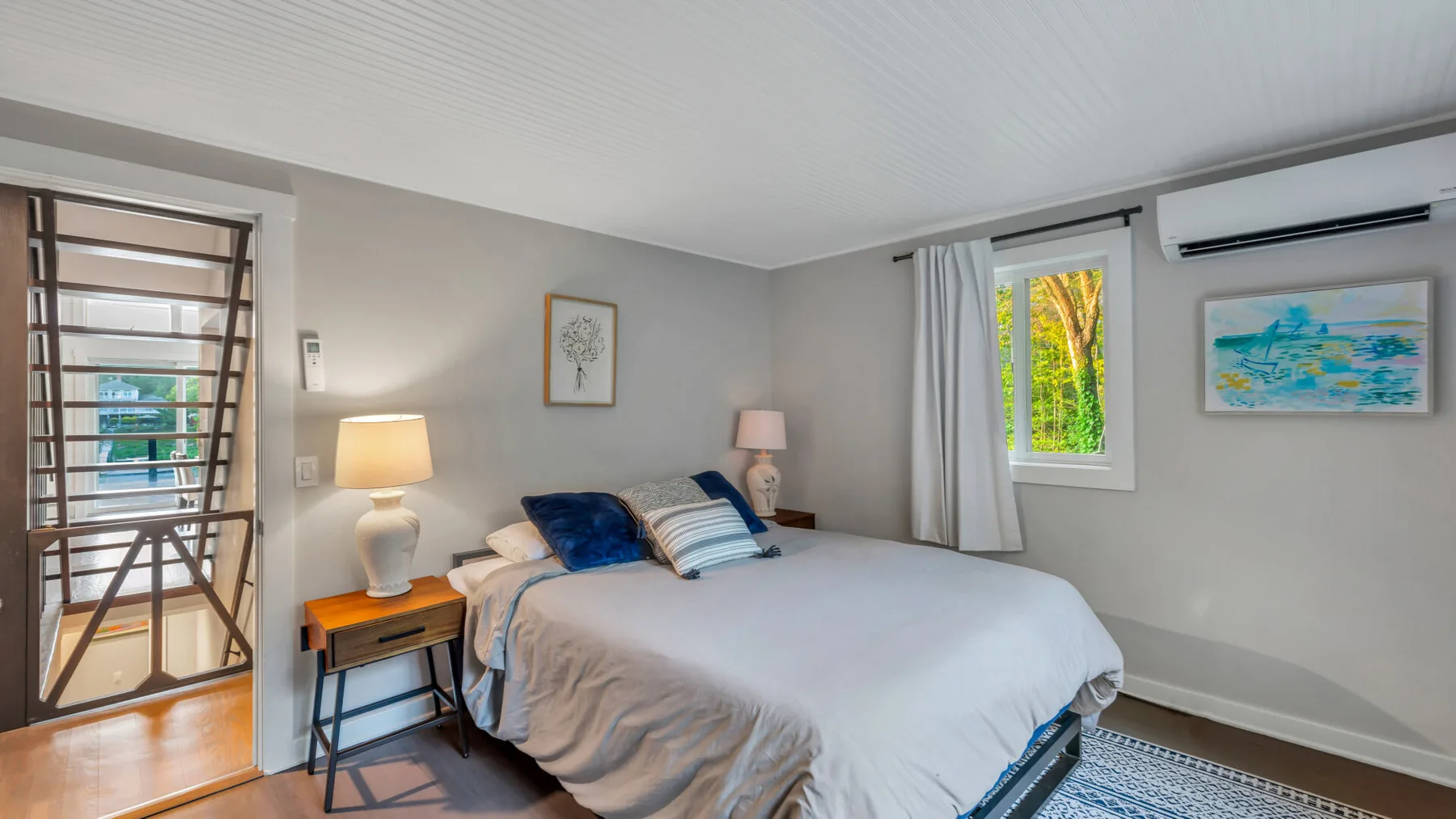 A bedroom with a neatly made bed and a window overlooking greenery.