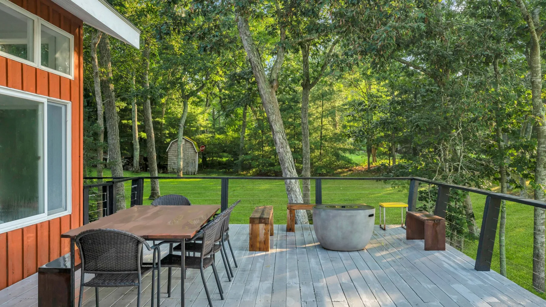 A wooden deck beside a house has outdoor seating and overlooks a leafy yard.