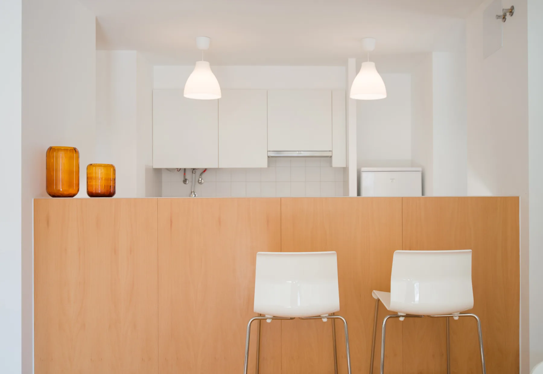 Una cocina luminosa con una barra de madera y dos taburetes blancos.