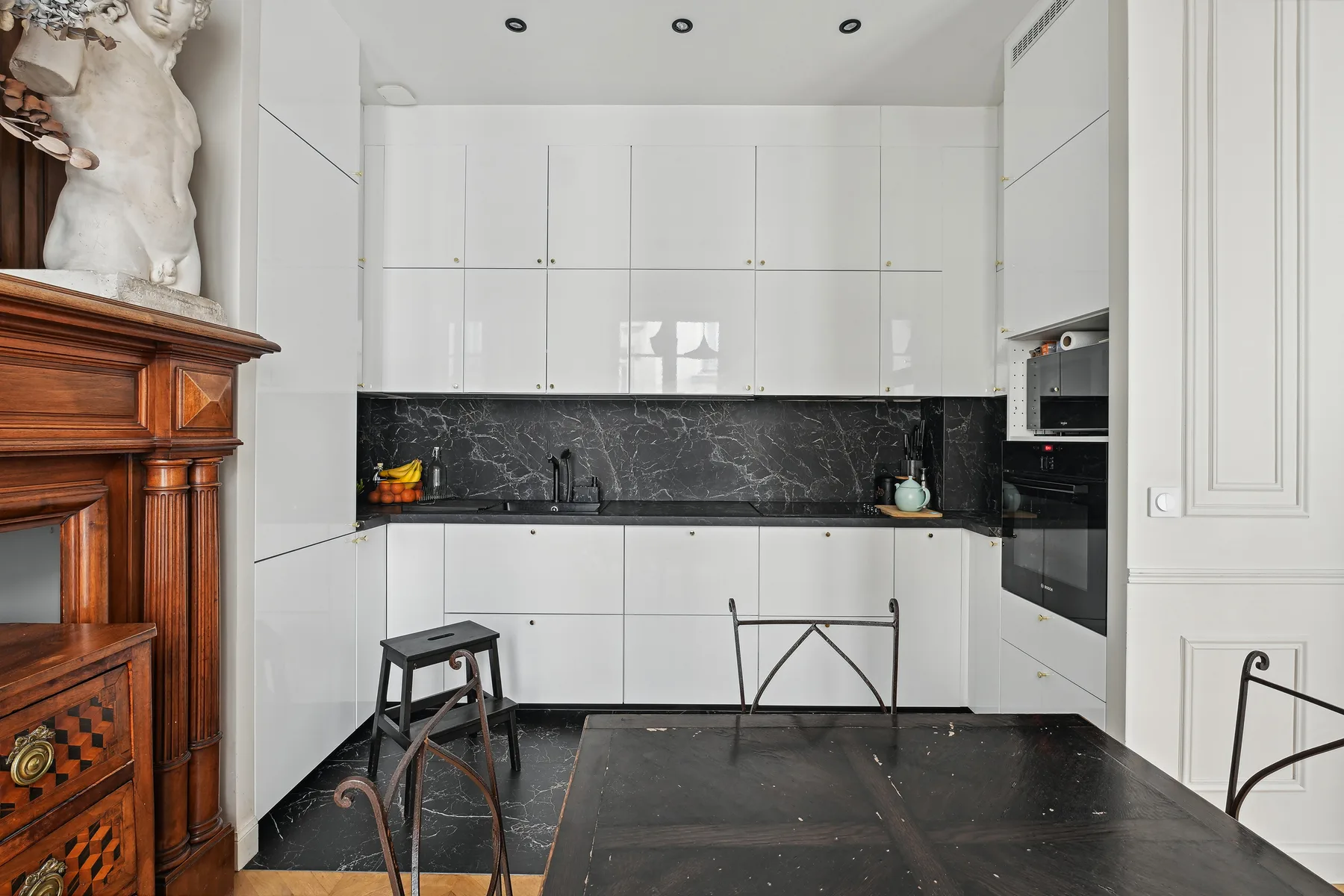 Una cocina blanca y luminosa con encimera oscura y mesa negra.