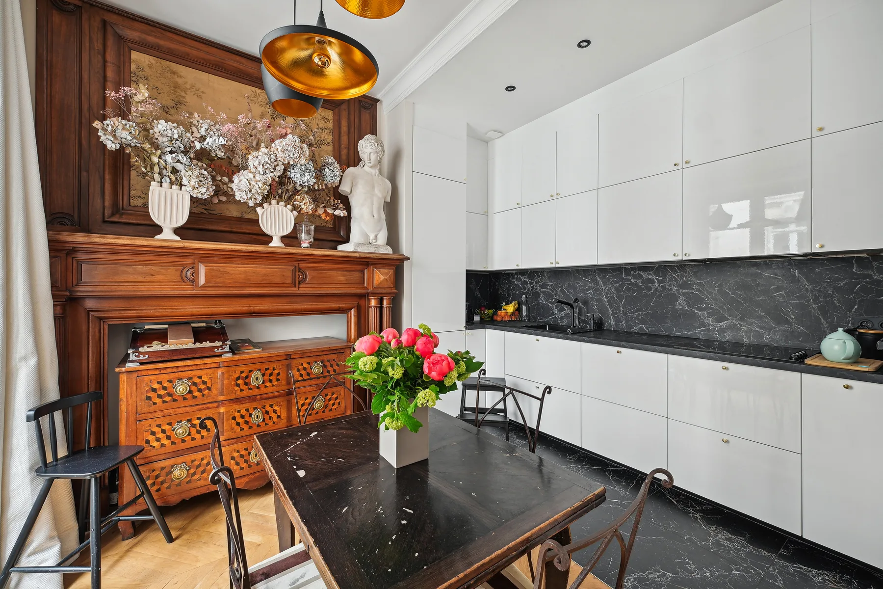 Un comedor con una mesa oscura y sillas junto a una cocina blanca.