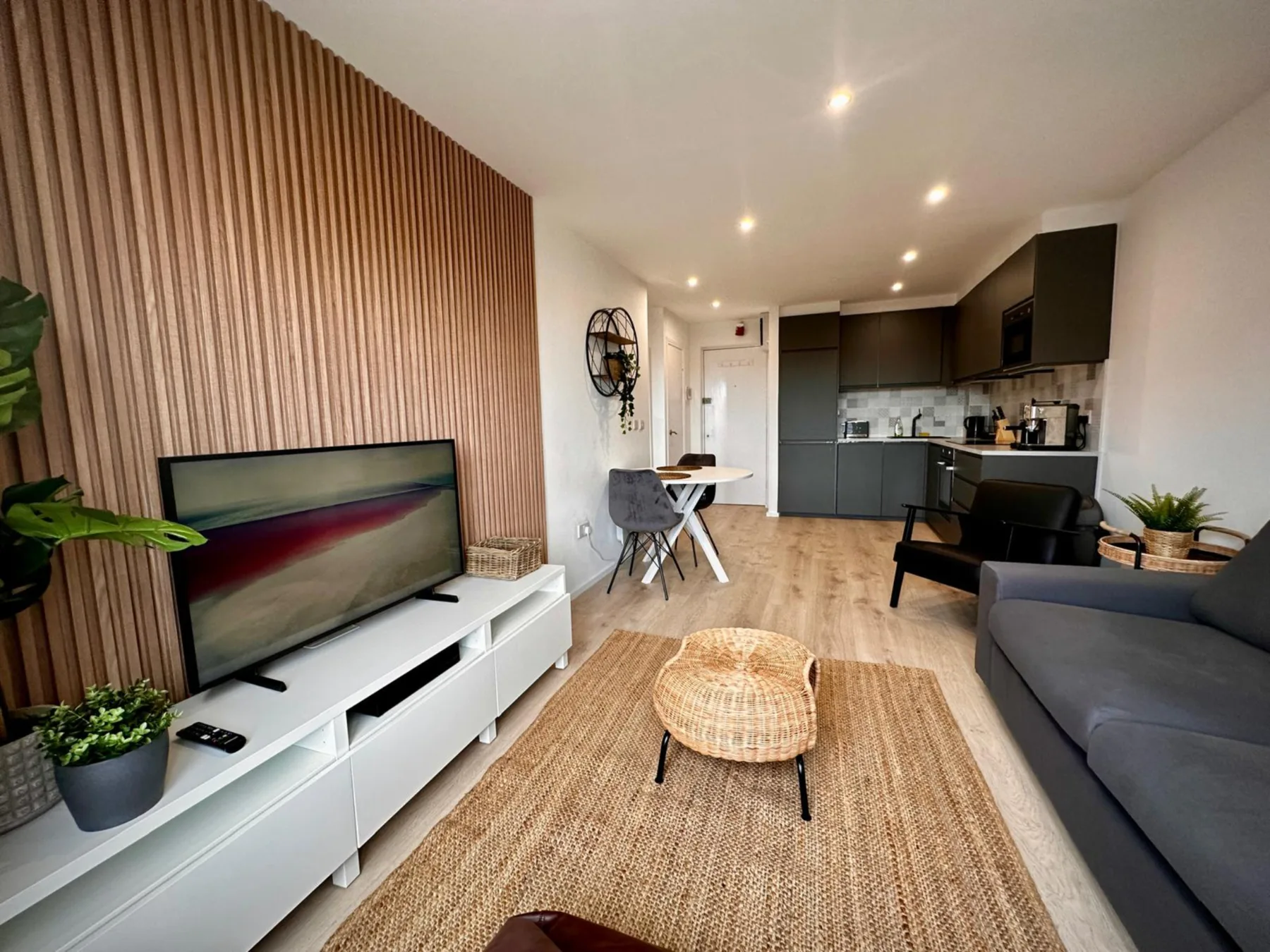 Sala de estar con televisor, asientos y una cocina abierta.