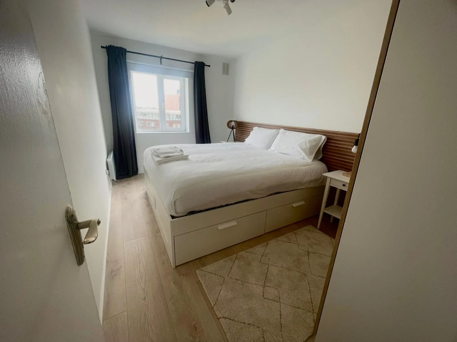 Un dormitorio con una cama junto a una ventana con cortinas oscuras.