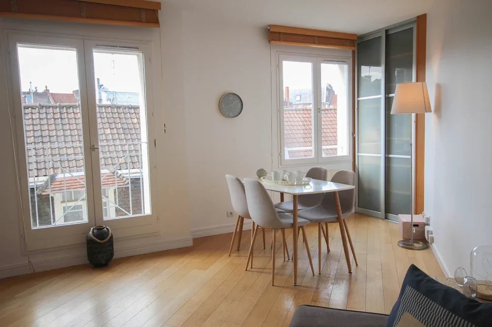 A bright dining area with a round table and windows overlooking rooftops.