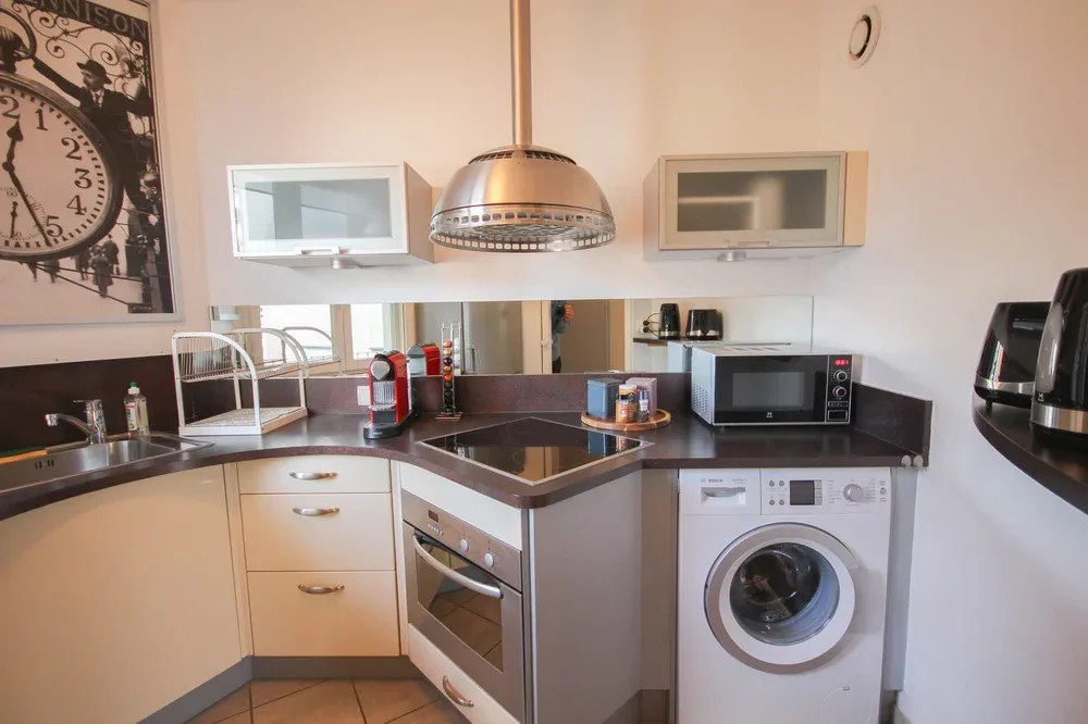 A compact kitchen with dark countertops, an oven, microwave, and washing machine.