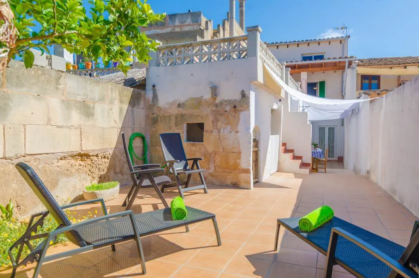 A sunny tiled patio with lounge seating and a leafy tree.