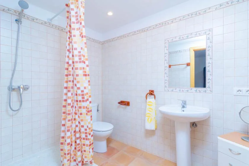 A tiled bathroom has a shower, toilet, and pedestal sink.