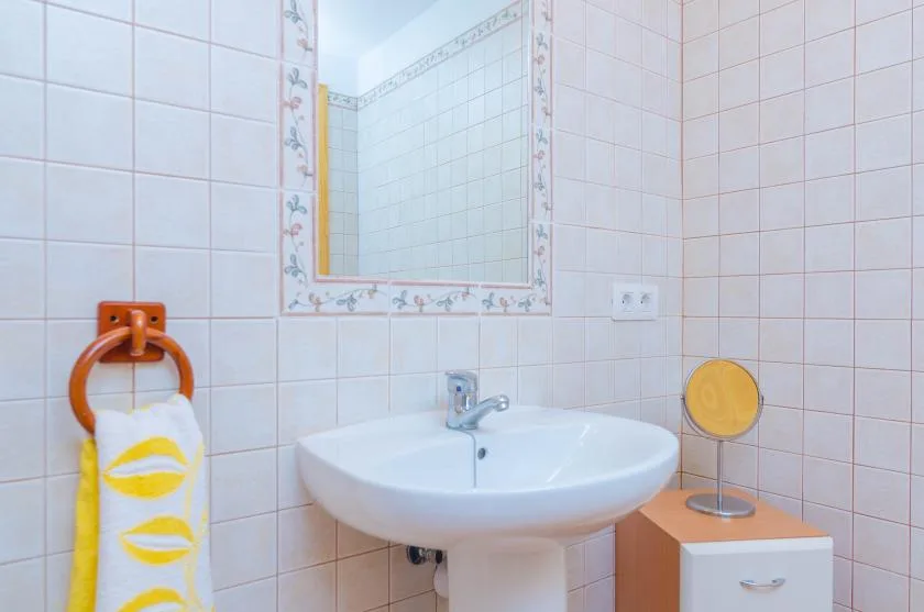 A tiled bathroom sink sits beneath a decorative mirror.
