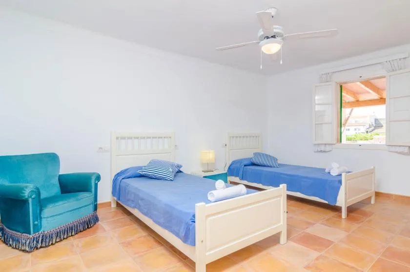 A bedroom with two beds and a teal armchair.