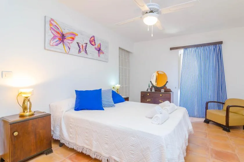 A bedroom with a white bed, blue curtains, and colorful butterfly artwork.