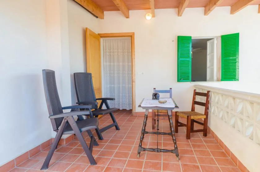 A covered terrace with seating and a small table beside an open window.