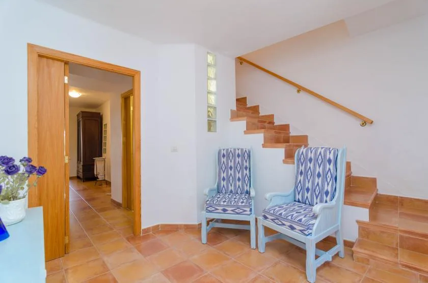 A bright interior hallway with a staircase and two patterned chairs.