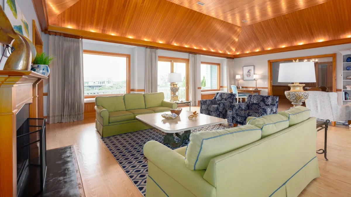 Una sala de estar con asientos verdes, una mesa de centro y un techo revestido de madera.