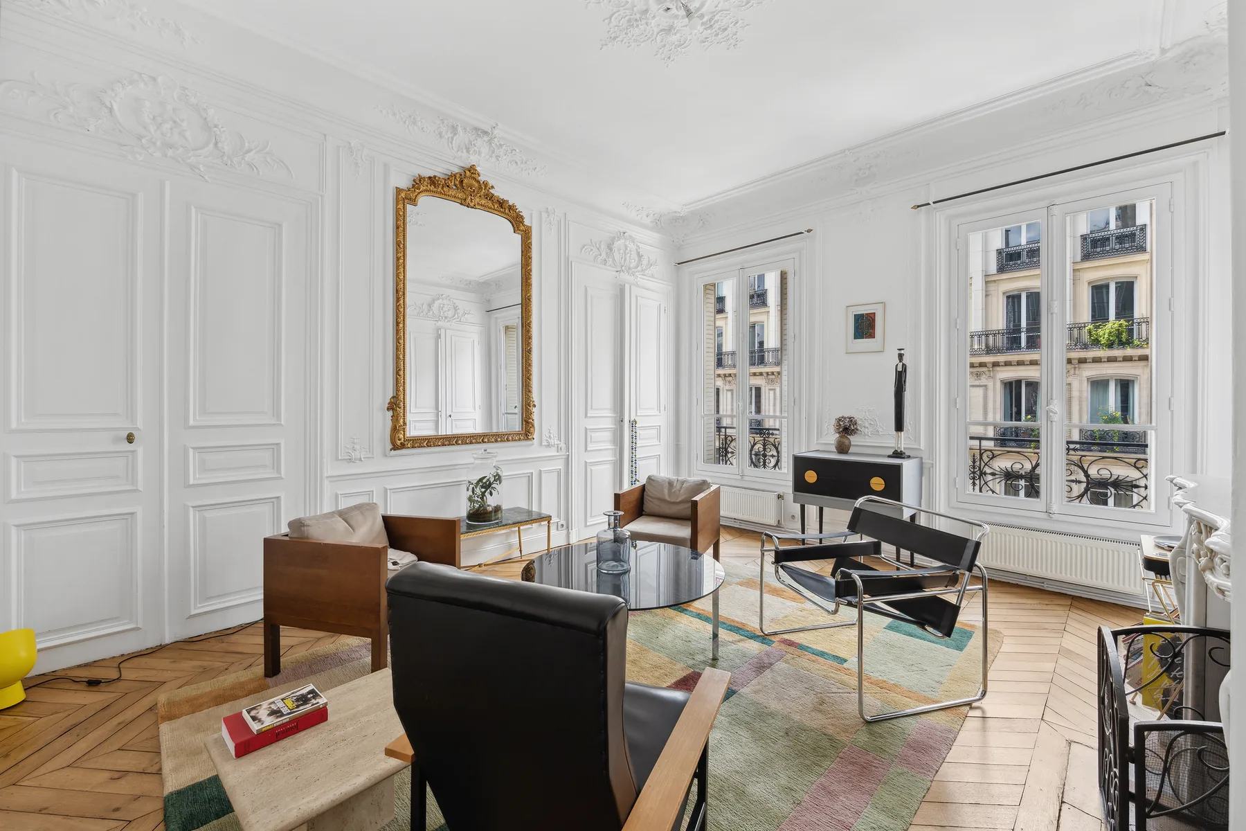 A bright living room with seating, a glass coffee table, and tall windows.