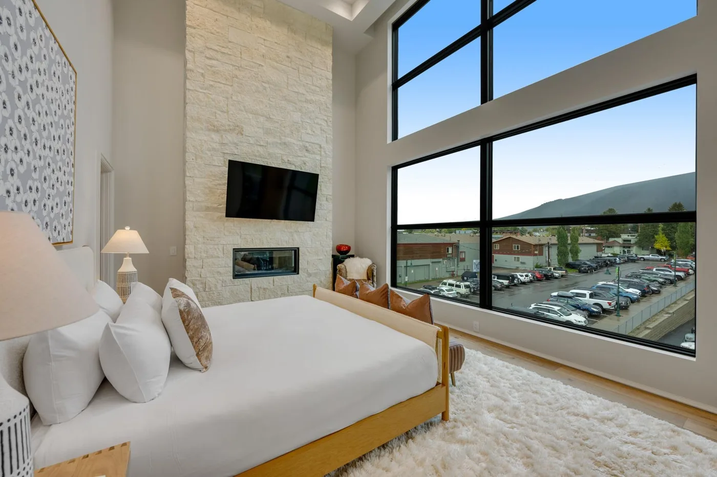 A bright bedroom with a large bed, a stone feature wall, and expansive windows.