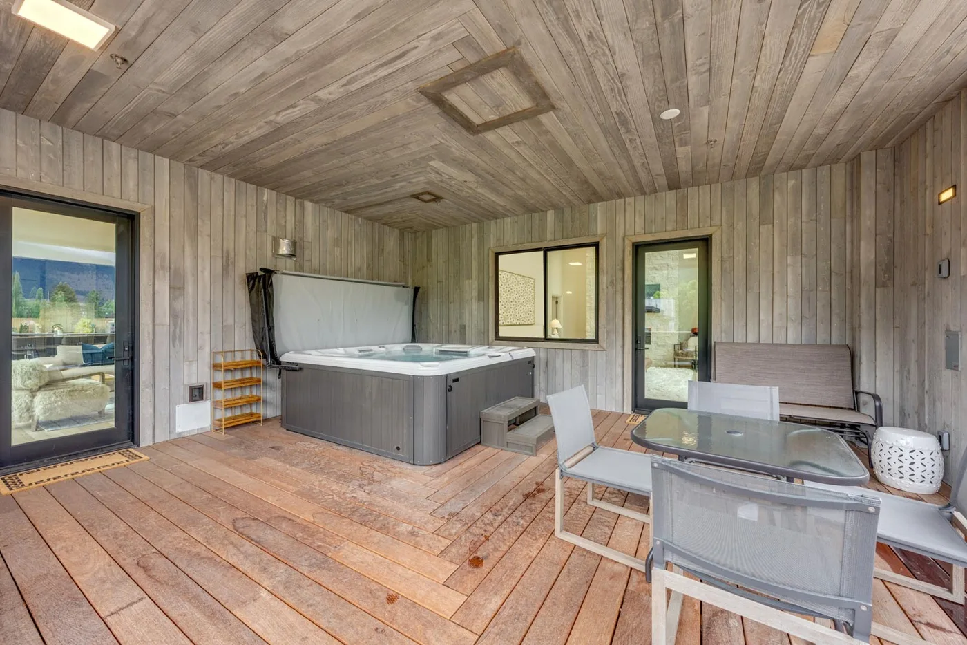 A covered patio with a hot tub and outdoor dining table.