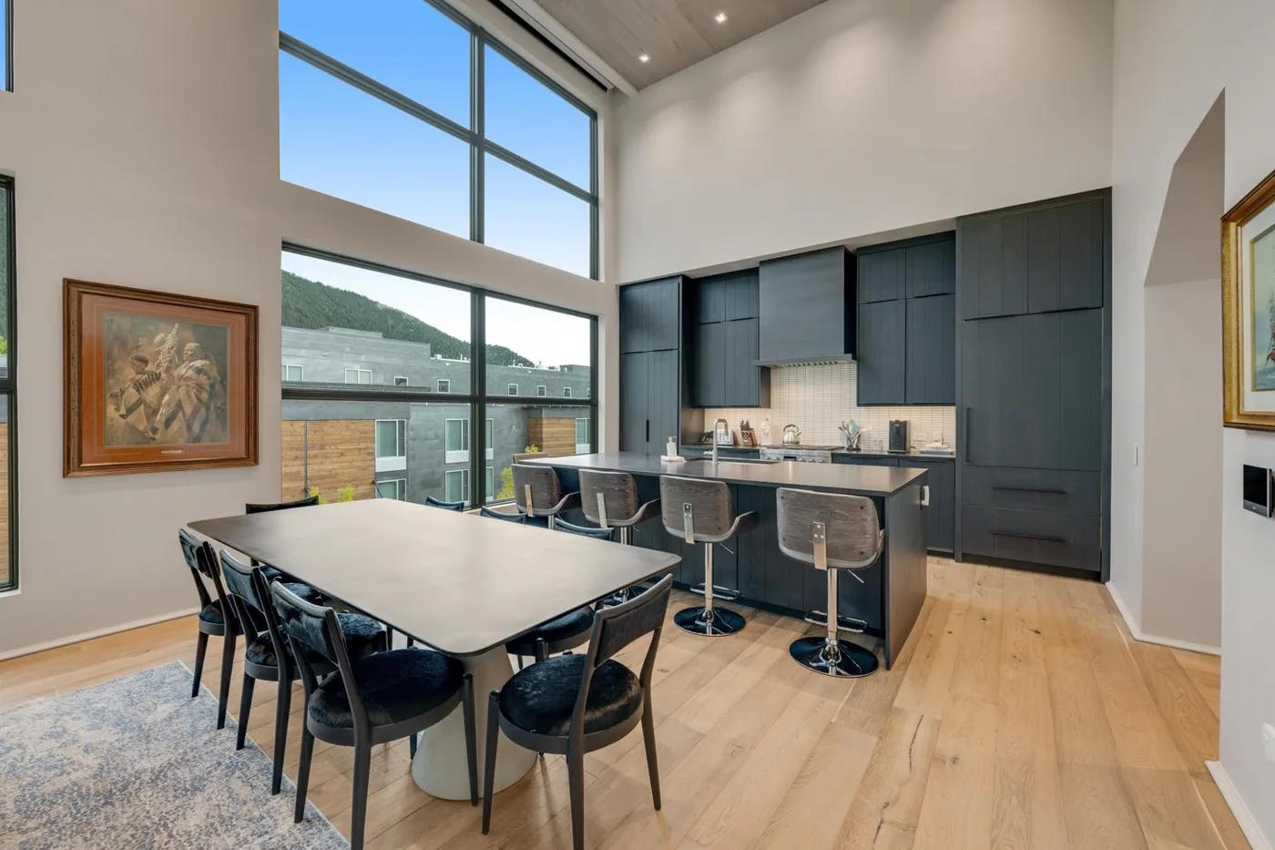 A dining area opens onto a kitchen beneath tall windows.