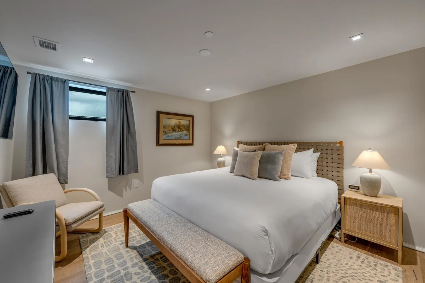 A bedroom with a neatly made bed, bedside lamps, and a window with curtains.