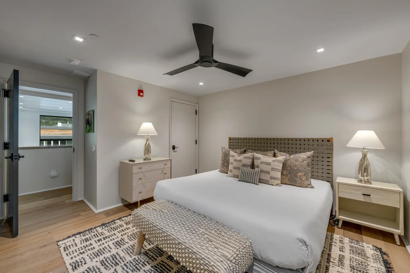 A bedroom with a bed, bedside tables, and a woven bench at its foot.