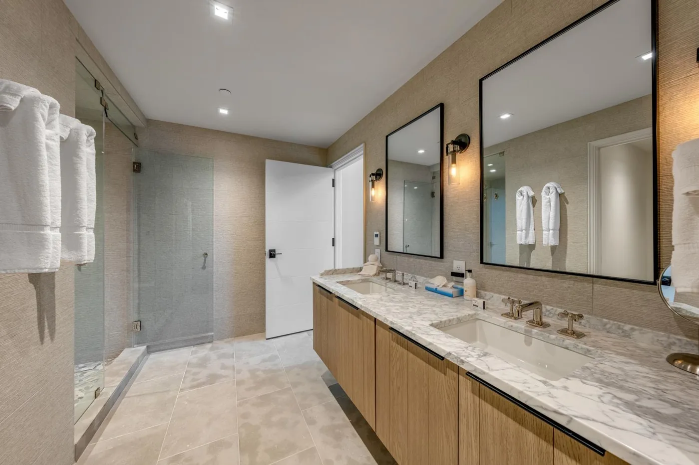 A bright bathroom with a glass shower and a long double-sink vanity.