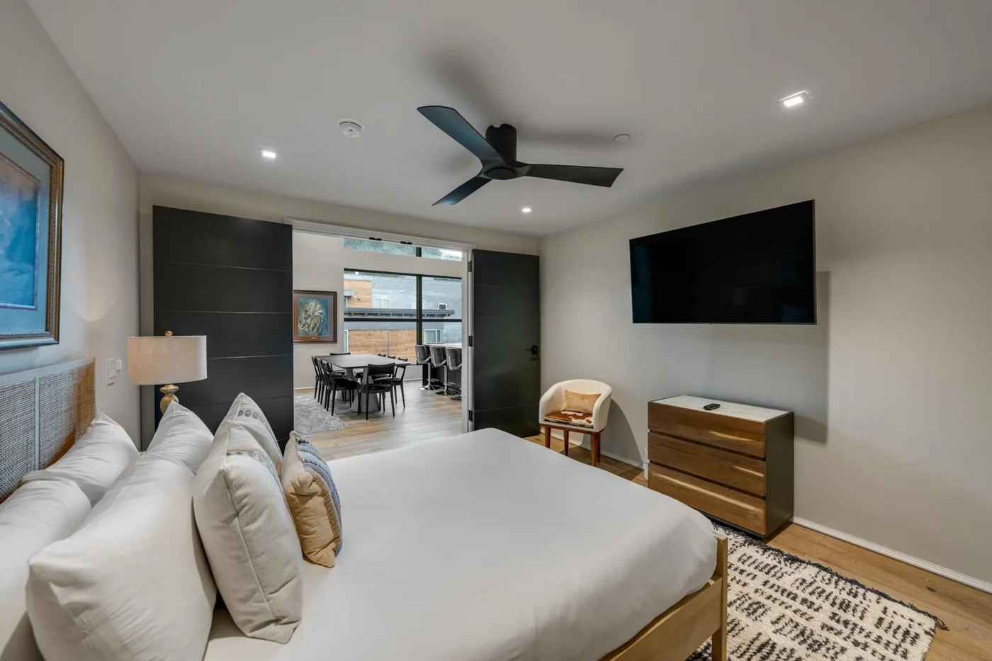 A bedroom with a large bed, wall-mounted television, and seating area visible beyond the doorway.