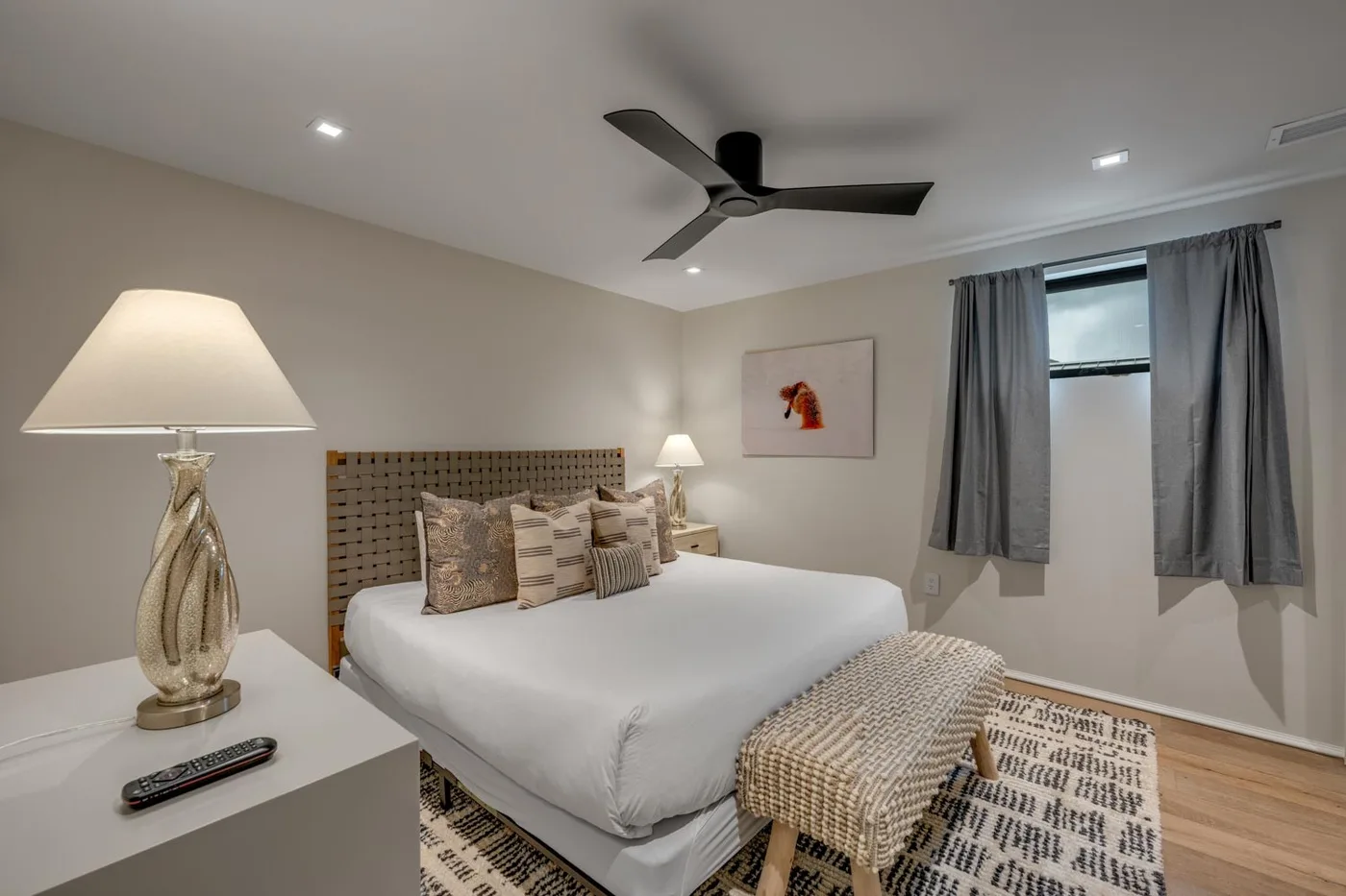 A bedroom with a neatly made bed, bedside tables, and a window with curtains.