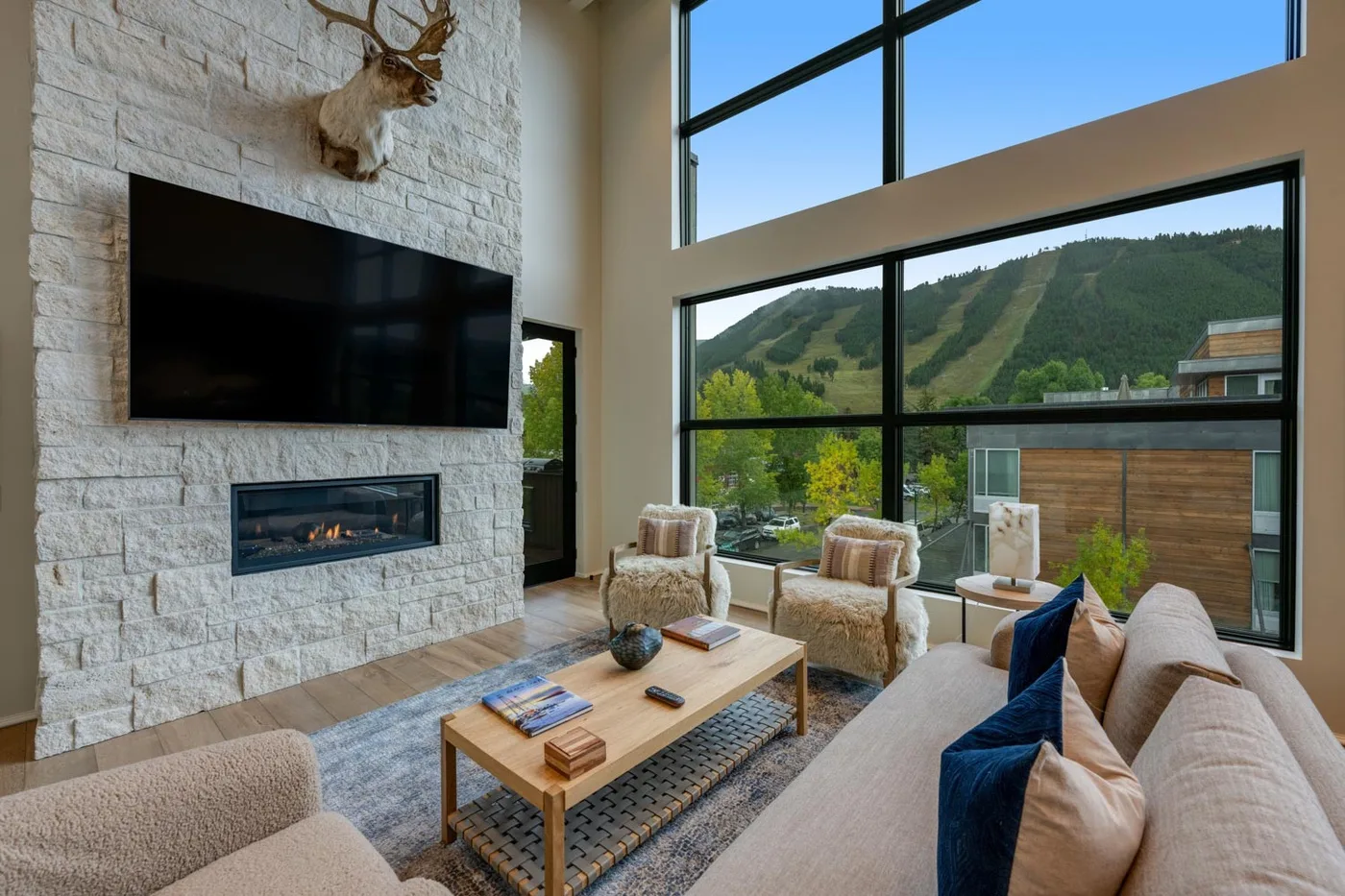 A living room with seating arranged around a coffee table beside large windows.