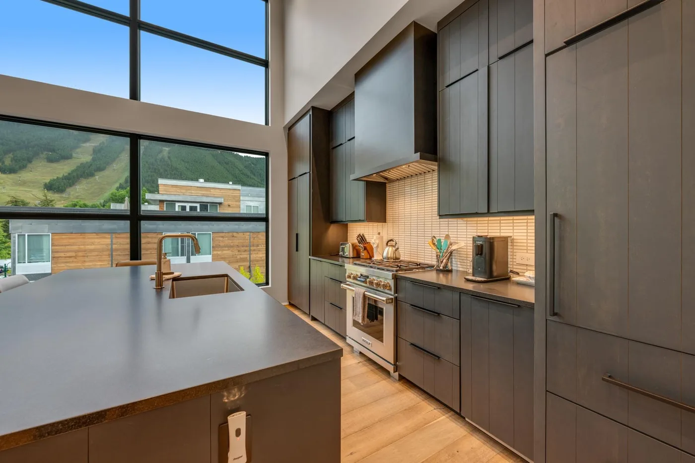 A modern kitchen with dark cabinetry, a central island, and large windows.