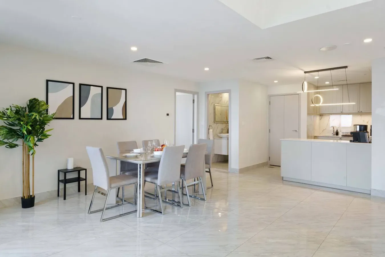 A bright open-plan dining area and kitchen with a table and white cabinetry.
