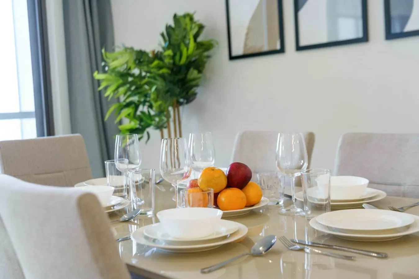 A dining table is set with plates and glassware beside a leafy plant.