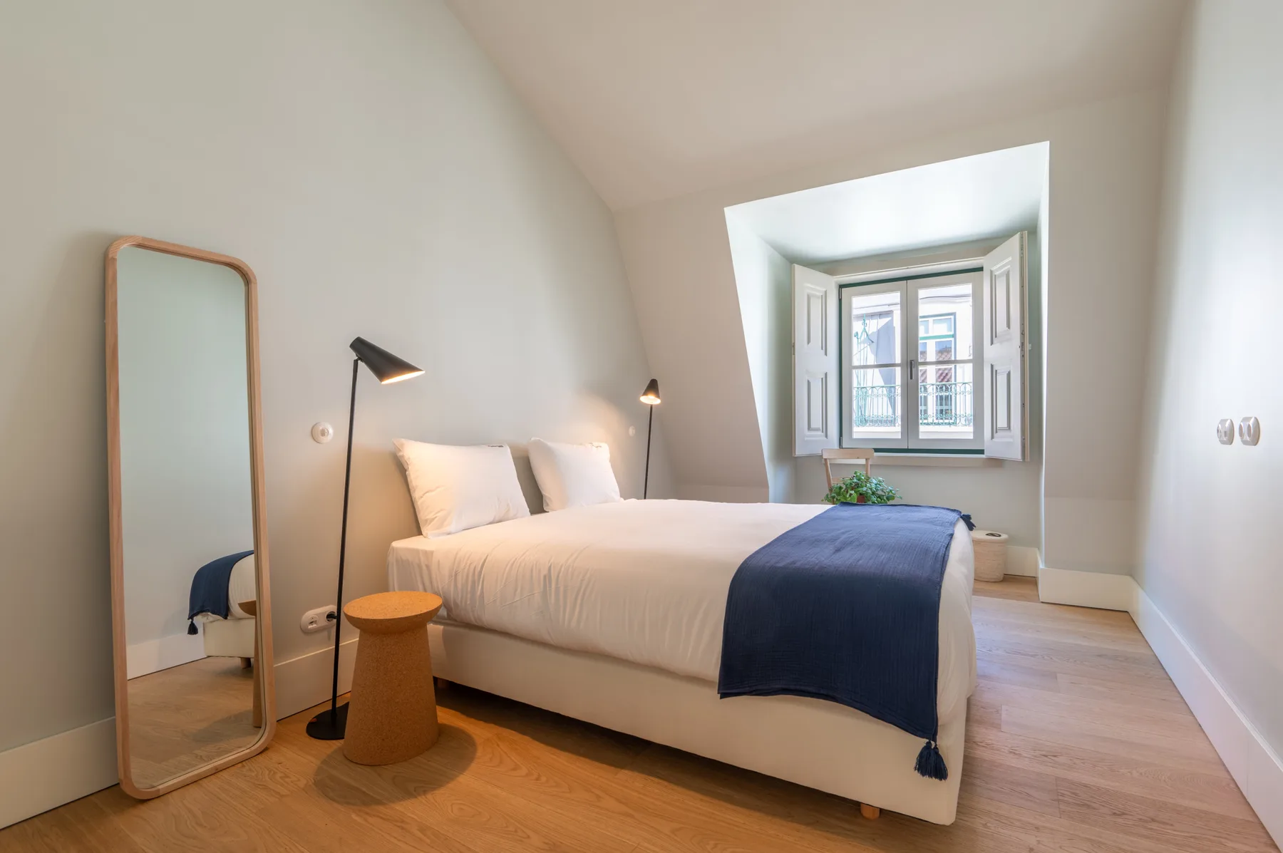 Un dormitorio luminoso con una cama bien tendida bajo una ventana.