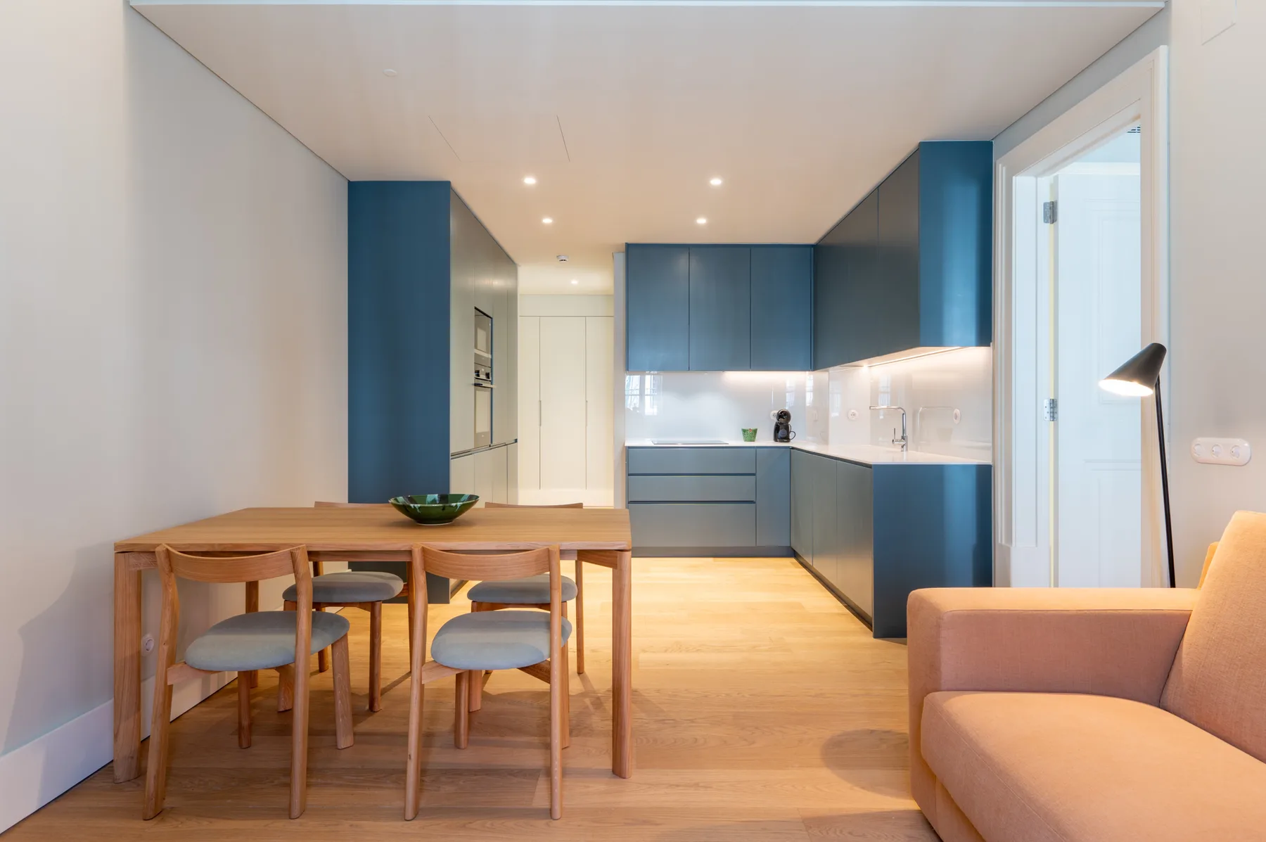 Zona de comedor y cocina con una mesa de madera y gabinetes azules.