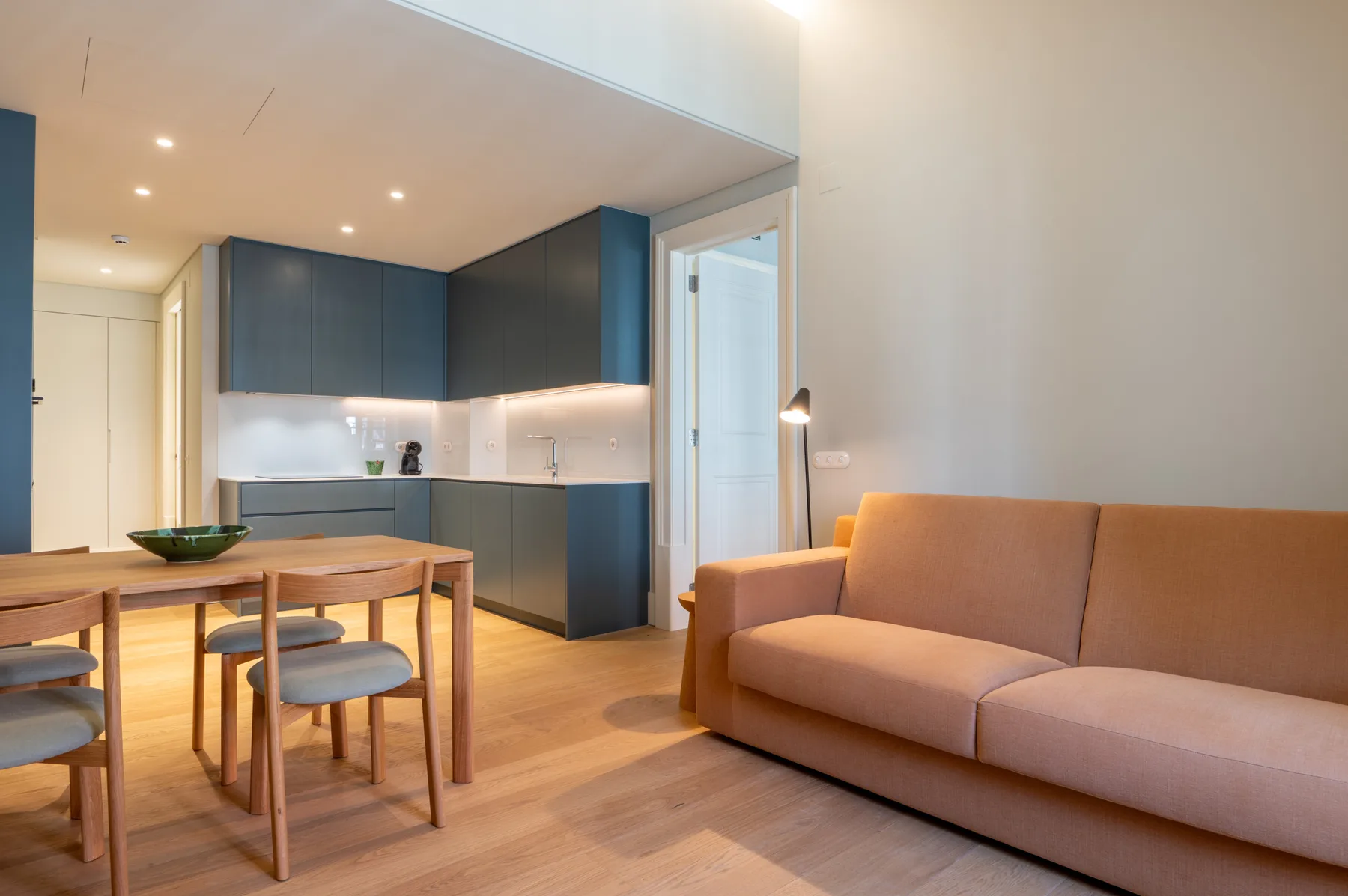 Una sala de estar y comedor moderna con sofá, mesa y cocina pequeña.