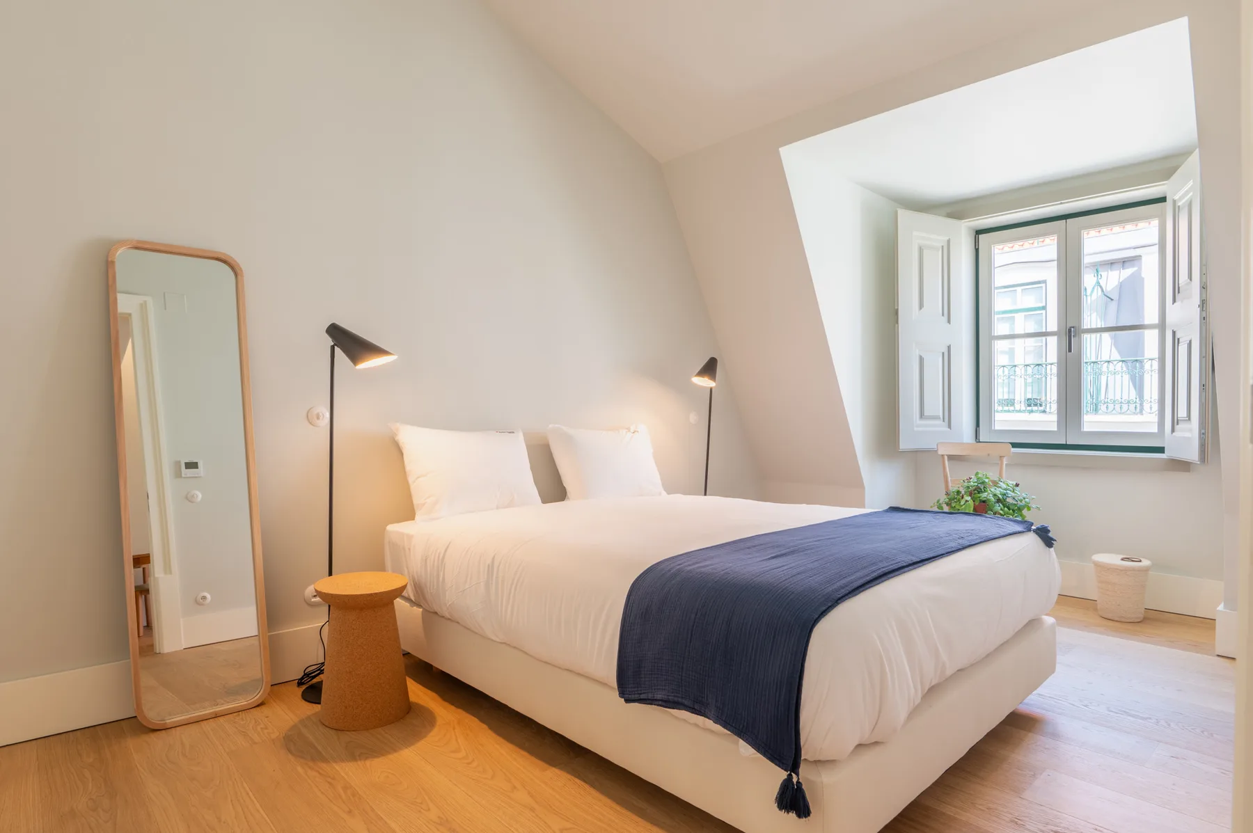 Un dormitorio luminoso con una cama, lámparas de noche y una ventana.