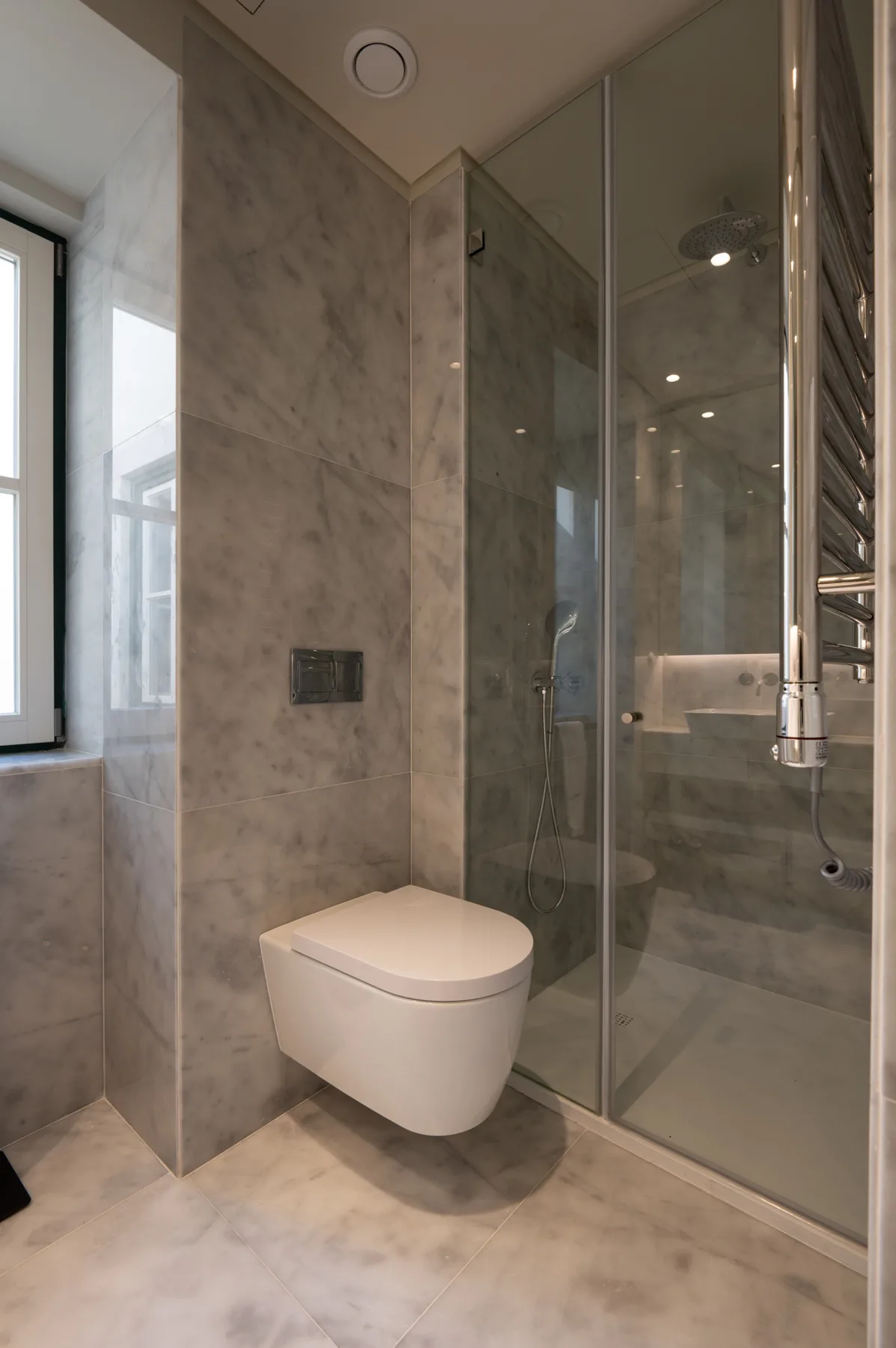 Un baño con azulejos, un inodoro suspendido y una ducha de vidrio.