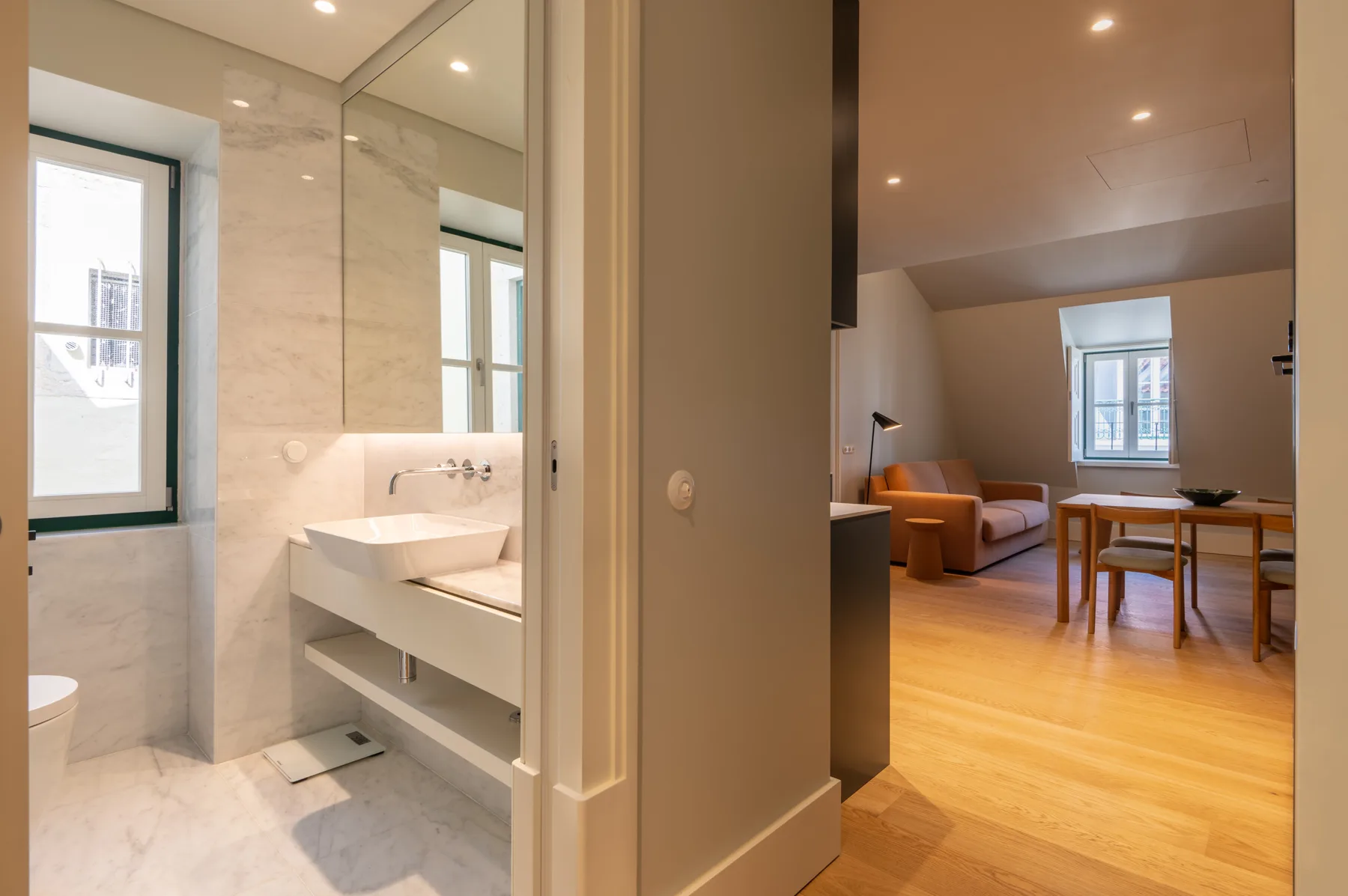 Un baño con lavabo se abre a una sala de estar con asientos y una mesa.