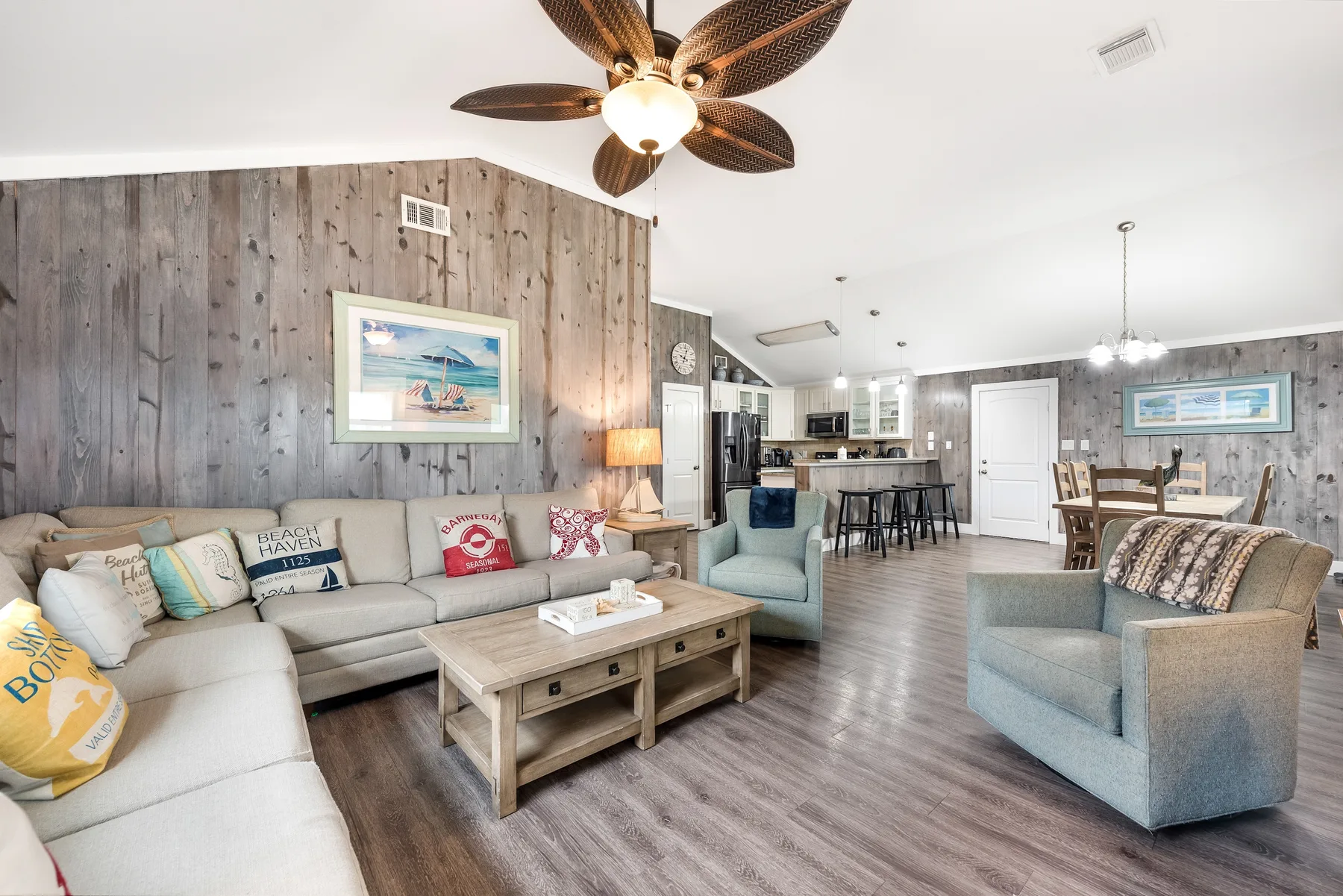 A living room with seating arranged around a coffee table, open to a kitchen.