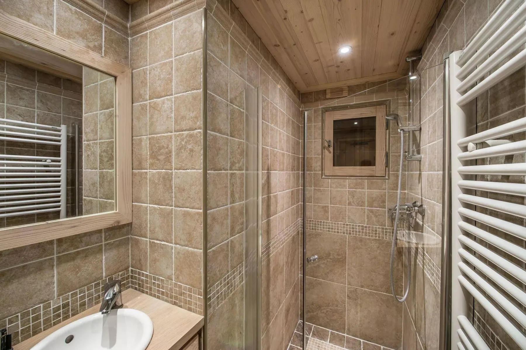 Un baño con azulejos, lavabo, ducha y techo de madera.