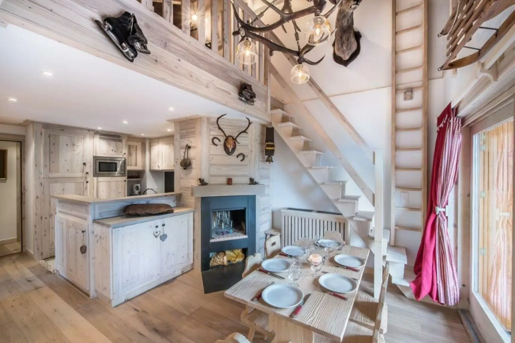 A rustic kitchen and dining area sits beneath a loft, with a staircase beside it.