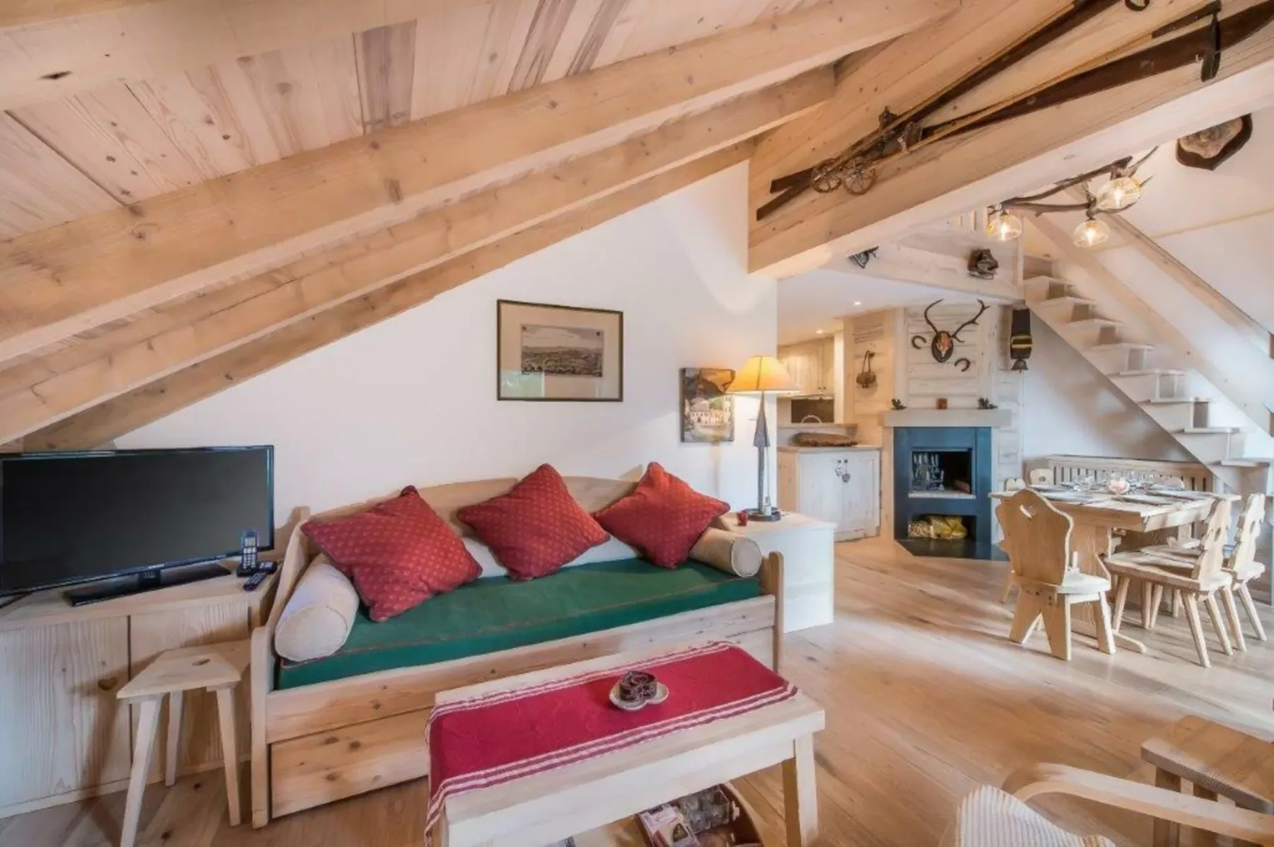 A cozy living area with a green sofa, television, and dining table beneath a wooden ceiling.
