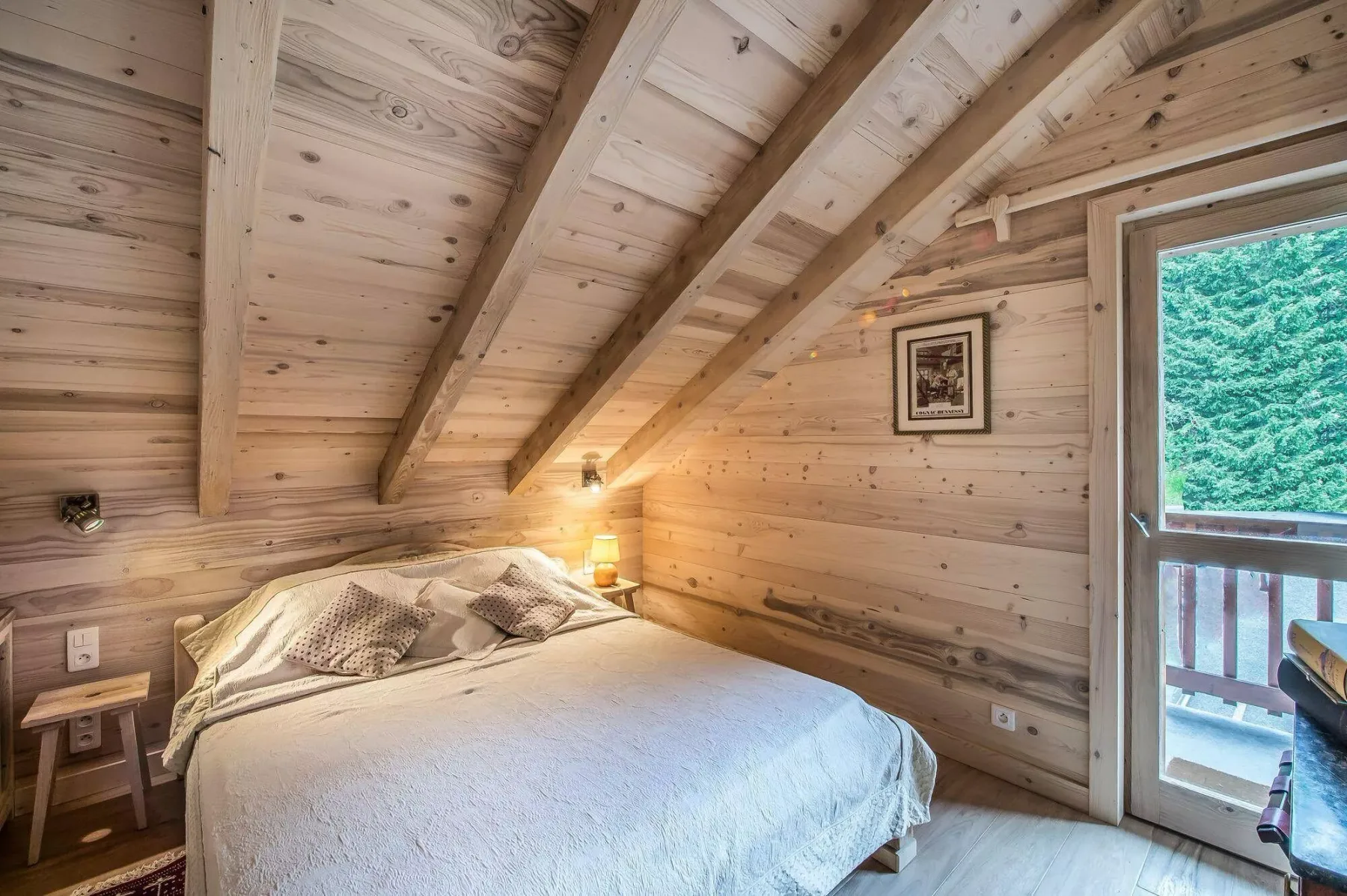 Dormitorio con una cama bajo un techo inclinado de madera y una puerta de vidrio.