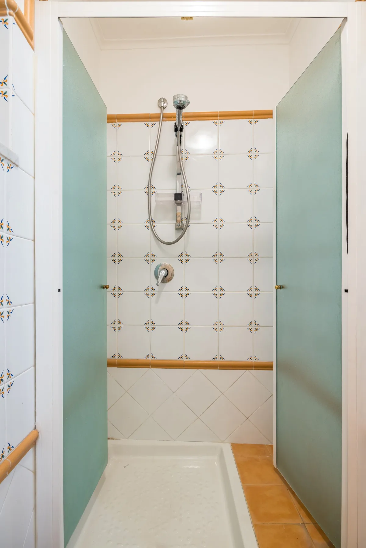 A tiled shower area with a handheld showerhead and pale green partition doors.