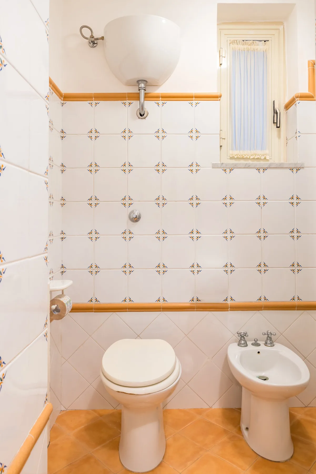 A tiled bathroom with a toilet, bidet, and wall-mounted sink.